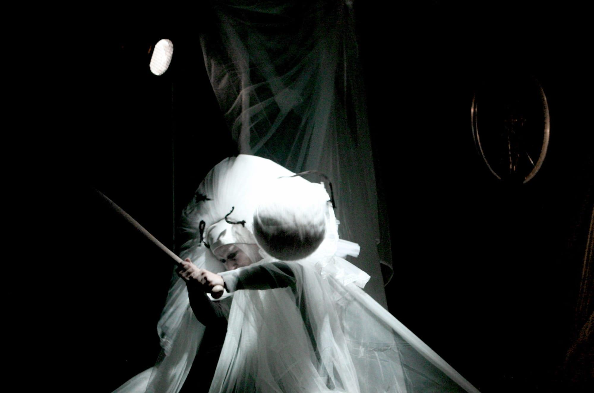 Una figura in abito bianco illuminata su un palco scuro.