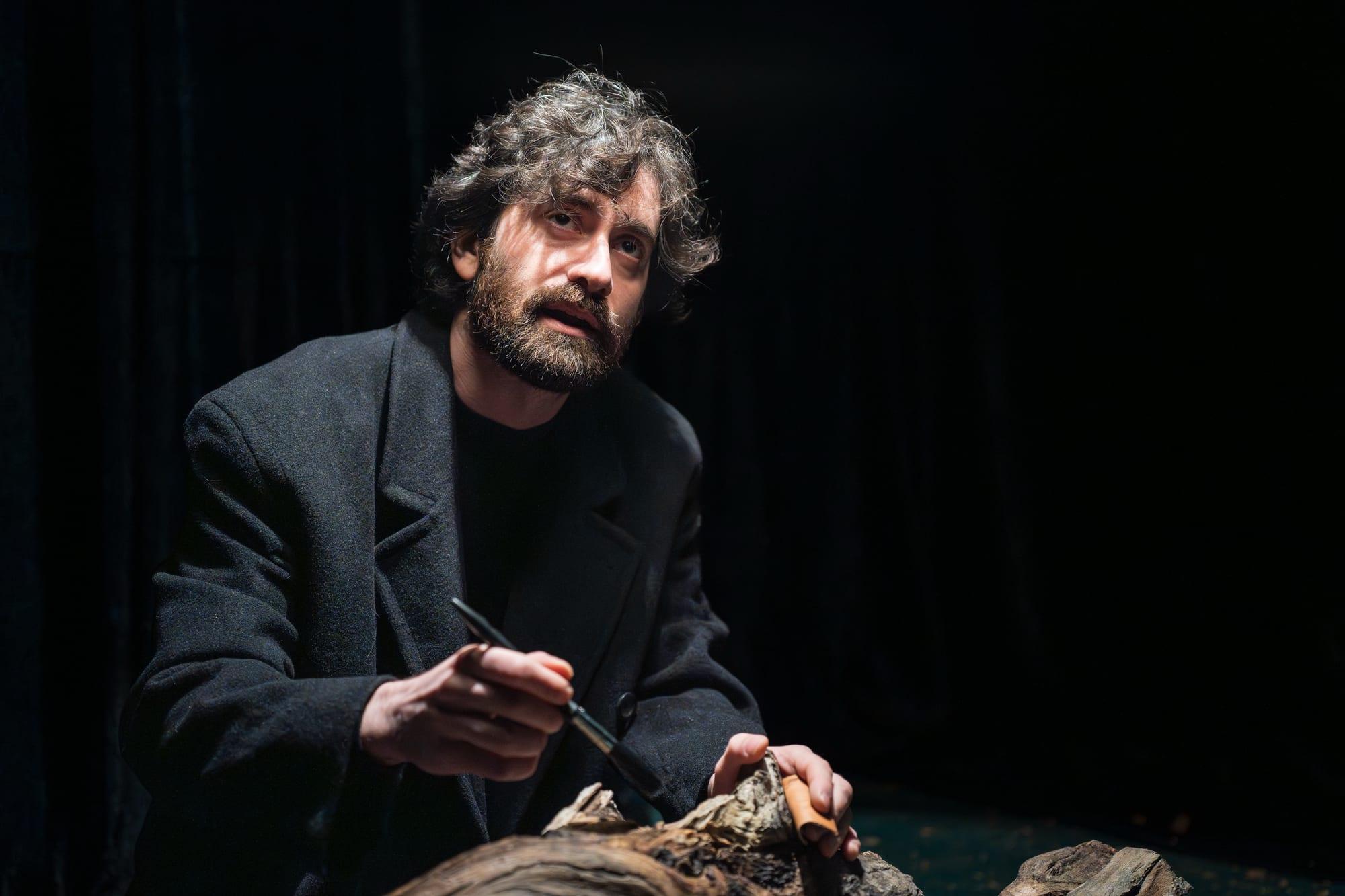 Un uomo seduto in scena, vestito di scuro.