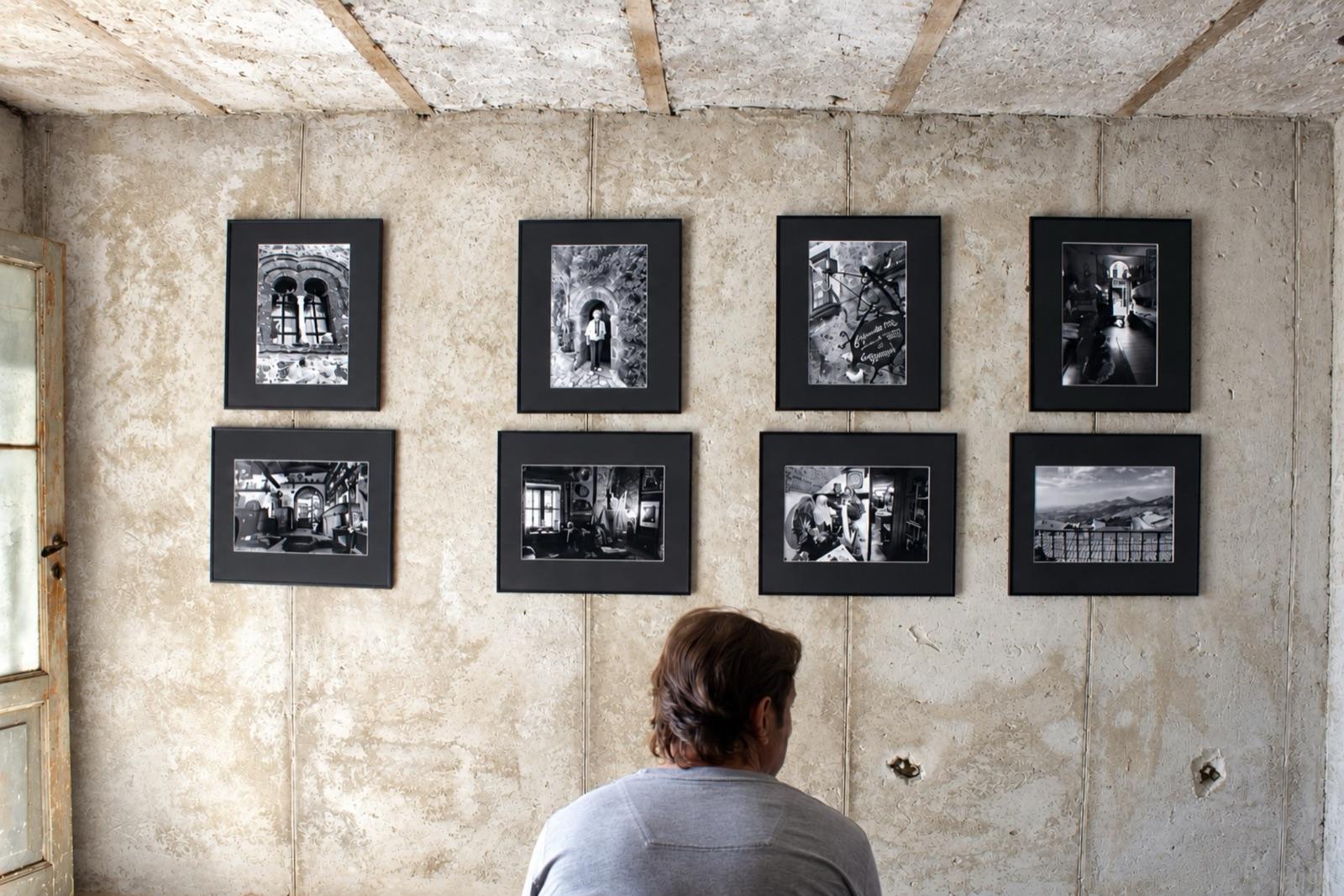 Una persona di spalle guarda otto fotografie in bianco e nero appese a una parete di cemento.